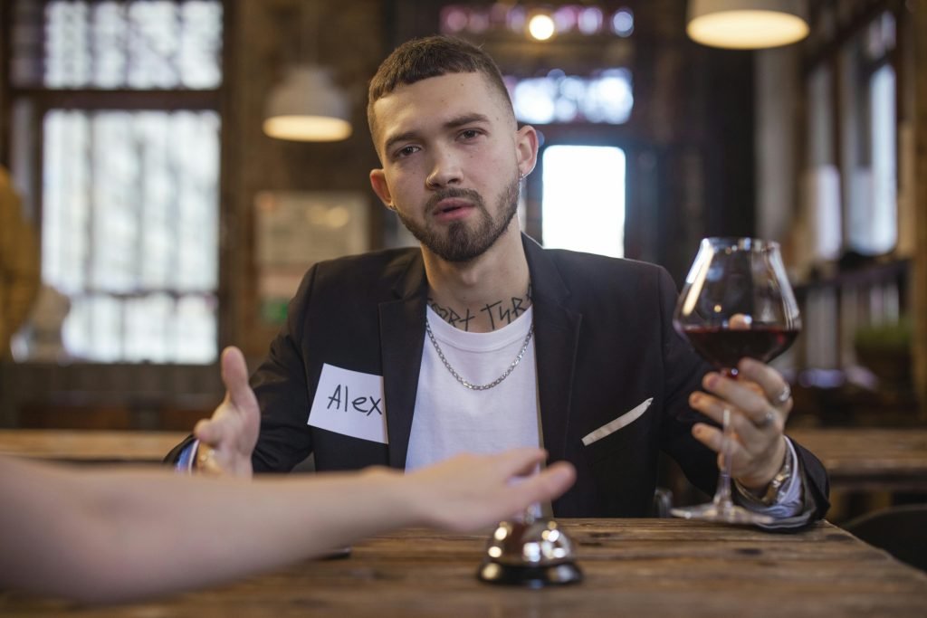 Man sitting indoors speed dating with name tag and wine glass.