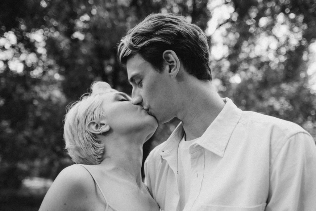 A couple shares an intimate kiss in a black and white outdoor setting, capturing romance and love.